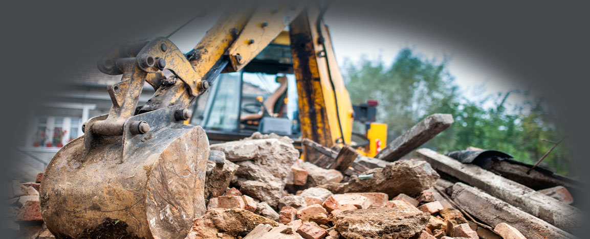 Excavator arm and bucket knocking down an old brick structure